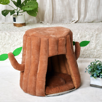 Dark grey plush cat house shaped like a tree stump, with an arched front opening and two branches with green leaves